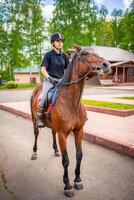 adorável jovem mulher vestindo capacete equitação dela Castanho cavalo foto