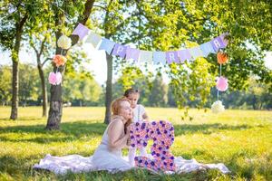 alegre mãe e filha tendo Diversão em criança aniversário em cobertor com papel decorações dentro a parque foto