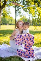 alegre mãe e filha tendo Diversão em criança aniversário em cobertor com papel decorações dentro a parque foto