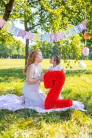 alegre mãe e filha tendo Diversão em criança aniversário em cobertor com papel decorações dentro a parque foto