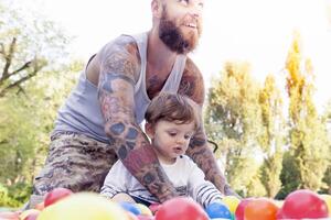 tatuado pai ter Diversão com dele filho dentro a parque com colori bolas foto