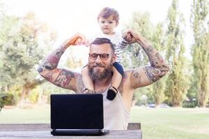 tatuado Papai ter Diversão com dele filho e computador portátil foto