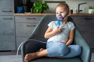 fofa pequeno menina estão sentado e segurando uma nebulizador mascarar inclinado contra a face às casa em doente deixar, via aérea tratamento conceito. Alto qualidade foto