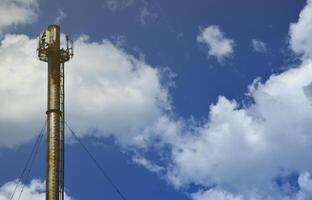 chaminé de metal alto da planta industrial com escada em forma de cintas de metal no contexto de um céu azul nublado foto