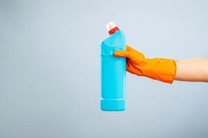 mão dentro luva segurando uma plástico detergente garrafa em azul fundo foto