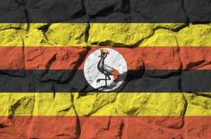 Uganda bandeira retratado dentro pintura cores em velho pedra parede fechar-se. texturizado bandeira em Rocha parede fundo foto