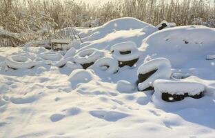 pneus de carros usados e descartados ficam na beira da estrada, cobertos com uma espessa camada de neve foto