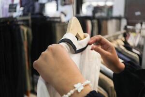 uma cliente é escolhendo a partir de uma linha do roupas suspensão em uma loja prateleira. adequado para moda e varejo conceitos foto