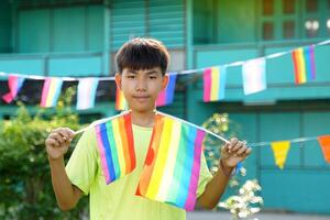 ásia Garoto detém uma arco Iris bandeira dentro frente do uma casa decorado com arco Iris bandeiras durante orgulho mês para mostrar lgbt orgulho e identidade. suave e seletivo foco. foto