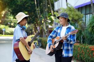 dois ásia Rapazes estavam tendo Diversão jogando clássico guitarra juntos durante seus livre Tempo às uma escola verão acampamento às a parque. suave e seletivo foco. foto