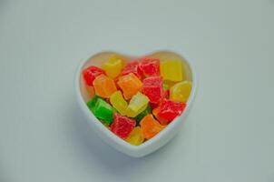 colorida cristalizado frutas dentro uma branco em forma de coração prato foto