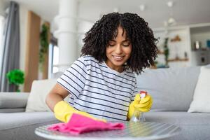 lindo jovem mulher faz limpeza a casa. menina esfrega pó. limpeza mesa e pulverização desinfetantes, usando limpeza soluções ou usando álcool para mate germes. foto