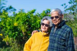 retrato do uma romântico idosos ásia casal sorridente e olhando às a Câmera enquanto em pé dentro uma jardim. Senior casal. conceito do envelhecido pessoas e cuidados de saúde foto