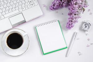 Primavera flatlay. bloco de anotações, computador portátil, lilás flores e copo do café em luz fundo. foto