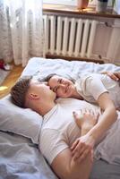jovem casal em a cama segurando mãos, uma menina em uma Rapazes ombro, concurso abraços e toques foto