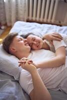 jovem casal em a cama segurando mãos, uma menina em uma Rapazes ombro, concurso abraços e toques foto