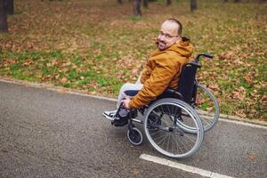 retrato do feliz paraplégico deficiente homem dentro cadeira de rodas dentro parque. ele é rolando em caminho. foto