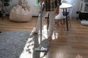 uma mulher aspiradores uma volta tapete dentro uma casa entre casa plantas com uma mão vácuo limpador. geral limpeza do a casa, limpeza serviço e dona de casa foto