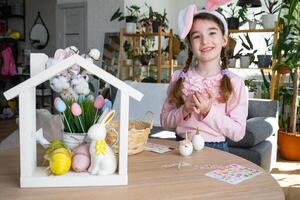 uma fofa menina com Rosa Coelho orelhas faz a Páscoa construir - decora a ovo dentro a Formato do uma unicórnio com strass, buzina, flores dentro a interior do uma casa com plantas. foto