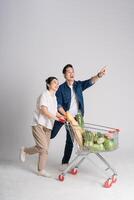 imagem do ásia casal empurrando supermercado carrinho enquanto compras, isolado em branco fundo foto