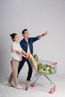 imagem do ásia casal empurrando supermercado carrinho enquanto compras, isolado em branco fundo foto