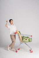sorridente mulher alegremente empurrando uma supermercado carrinho, isolado em branco fundo foto