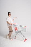 sorridente mulher alegremente empurrando uma supermercado carrinho, isolado em branco fundo foto