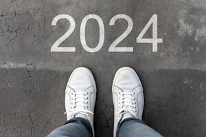 ai gerado número 2024 desenhado em rachado asfalto, pés dentro sapatos em pé em chão. conceito do a chegando Novo ano 2024. topo visualizar, pov, fechar-se foto