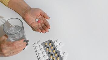 idosos mulher levando medicamento. fechar acima do fêmea mãos segurando vidro do água e pílulas, branco fundo cópia de espaço. tratamento conceito, doença aposentadoria foto