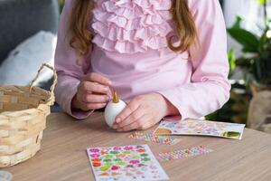 uma fofa menina com Rosa Coelho orelhas faz a Páscoa construir - decora a ovo dentro a Formato do uma unicórnio com strass, buzina, flores dentro a interior do uma casa com plantas. foto