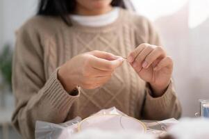 uma fechar-se imagem do uma mulher inserindo uma agulha, rosqueamento uma de costura agulha, de costura às lar. foto