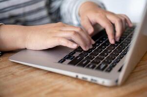 uma fechar-se tiro do uma mulher trabalhando em dela computador portátil computador às dela mesa, digitando em computador portátil teclado. foto