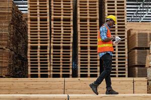 africano trabalhadores homem Engenharia caminhando e inspecionando com trabalhando suíte vestir e mão luva dentro madeira madeira armazém. conceito do inteligente indústria trabalhador operativo. madeira fábricas produzir madeira palato. foto