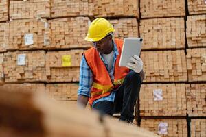 africano trabalhadores homem Engenharia caminhando e inspecionando com trabalhando suíte vestir e mão luva dentro madeira madeira armazém. conceito do inteligente indústria trabalhador operativo. madeira fábricas produzir madeira palato. foto