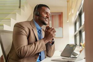 cliente Apoio, suporte ligar Centro operador ou recepcionista. cliente serviço e homem consultor falando enquanto fazendo uma consulta on-line. africano operador masculino telemarketing agente em uma computador portátil dentro escritório foto