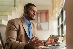 cliente Apoio, suporte ligar Centro operador ou recepcionista. cliente serviço e homem consultor falando enquanto fazendo uma consulta on-line. africano operador masculino telemarketing agente em uma computador portátil dentro escritório foto