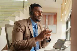 cliente Apoio, suporte ligar Centro operador ou recepcionista. cliente serviço e homem consultor falando enquanto fazendo uma consulta on-line. africano operador masculino telemarketing agente em uma computador portátil dentro escritório foto