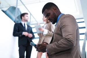 inteligente Preto homem de negocios assistindo Móvel telefone. Careca adulto homem vestindo formal vestir. pensativo afro-americano homem de negocios dentro uma perfeitamente sob medida terno em pé dentro escada dentro escritório. foto