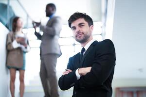 o negócio pessoas e escritório conceito. feliz sorridente homem de negocios dentro Sombrio terno. retrato do sorridente meio adulto homem de negocios em pé às corporativo escritório. homem de negocios sorridente com braços cruzado dentro escritório. foto