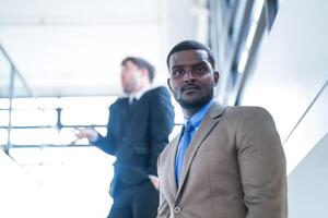 o negócio pessoas e escritório conceito. feliz sorridente homem de negocios dentro Sombrio terno. retrato do sorridente meio adulto homem de negocios em pé às corporativo escritório. homem de negocios sorridente com braços cruzado dentro escritório. foto