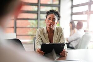 africano Preto o negócio mulher usando Smartphone enquanto trabalhando em computador portátil às escritório. sorridente maduro africano americano empresária olhando acima enquanto trabalhando em telefone. bem sucedido mulher empreendedor. foto