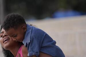 misturado raça africano e ásia mãe e Garoto é jogando às a ao ar livre área. sorridente feliz família ter Diversão corrida em a de praia. retrato do mãe e criança estilo de vida com uma único Penteado. foto