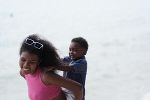 misturado raça africano e ásia mãe e Garoto é jogando às a ao ar livre área. sorridente feliz família ter Diversão corrida em a de praia. retrato do mãe e criança estilo de vida com uma único Penteado. foto