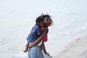 misturado raça africano e ásia mãe e Garoto é jogando às a ao ar livre área. sorridente feliz família ter Diversão corrida em a de praia. retrato do mãe e criança estilo de vida com uma único Penteado. foto