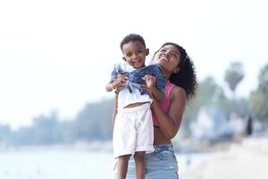 misturado raça africano e ásia mãe e Garoto é jogando às a ao ar livre área. sorridente feliz família ter Diversão corrida em a de praia. retrato do mãe e criança estilo de vida com uma único Penteado. foto