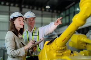 fábrica engenheiros inspecionando em máquina com inteligente tábua. trabalhador trabalho às pesado máquina robô braço. a Soldagem máquina com uma controlo remoto sistema dentro a industrial fábrica. artificial inteligência conceito. foto