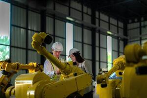 fábrica engenheiros inspecionando em máquina com inteligente tábua. trabalhador trabalho às pesado máquina robô braço. a Soldagem máquina com uma controlo remoto sistema dentro a industrial fábrica. artificial inteligência conceito. foto