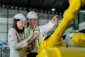 fábrica engenheiros inspecionando em máquina com inteligente tábua. trabalhador trabalho às pesado máquina robô braço. a Soldagem máquina com uma controlo remoto sistema dentro a industrial fábrica. artificial inteligência conceito. foto