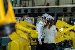 fábrica engenheiros inspecionando em máquina com inteligente tábua. trabalhador trabalho às pesado máquina robô braço. a Soldagem máquina com uma controlo remoto sistema dentro a industrial fábrica. artificial inteligência conceito. foto