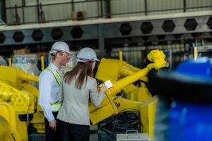 fábrica engenheiros inspecionando em máquina com inteligente tábua. trabalhador trabalho às pesado máquina robô braço. a Soldagem máquina com uma controlo remoto sistema dentro a industrial fábrica. artificial inteligência conceito. foto